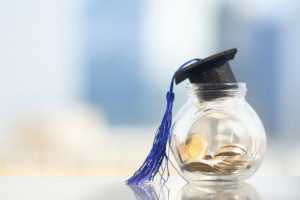 small graduation hat on top of a glass jar filled with coins representing saving money for college
